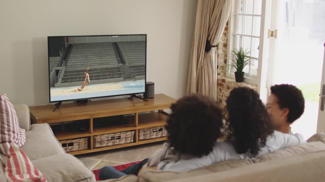 Composizione: famiglia felice seduta a casa insieme che guarda l'atletica del salto in lungo in TV.