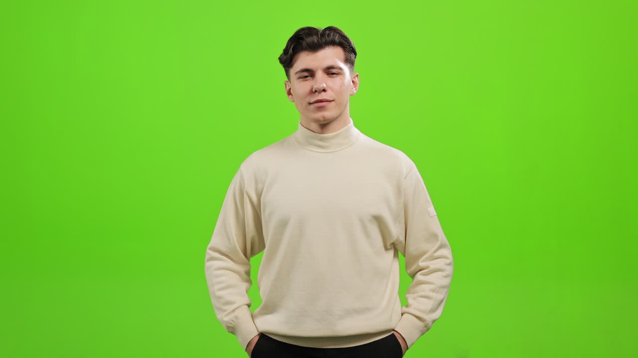 The man is standing and looking at the camera. He is putting his hands in his pockets. He is standing on a green background. Green screen. 4K.
