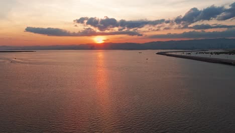 Breathtaking drone shot of a glowing sunset over a winding coastal road, calm waters, and distant skyline in the Philippines