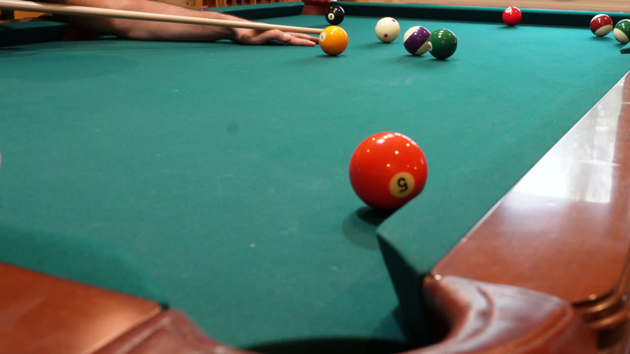 Man Playing 8 Ball Pool Shoots Brown Striped 15 Ball into Corner Pocket on a Brunswick Table with Green Felt using Draw or Backspin on the Cue Ball, Open Bridge Hand and Wooden Cue Stick, Low Angle