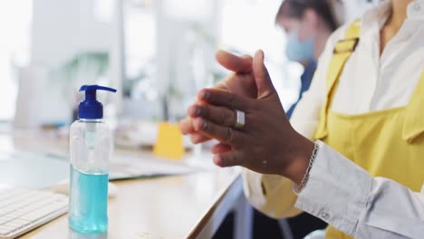 Mid-section-of-woman-sanitizing-her-hands-at-office