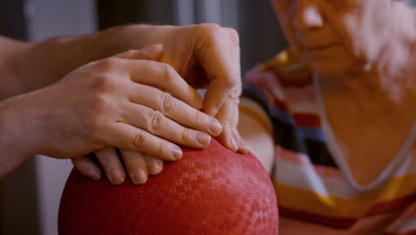 male caregiver gently assists the hemiplegic right hand ball therapy of an elderly female stroke survivor, seated across from him on glass top kitchen table at home. side to side motion of hand 24fps.