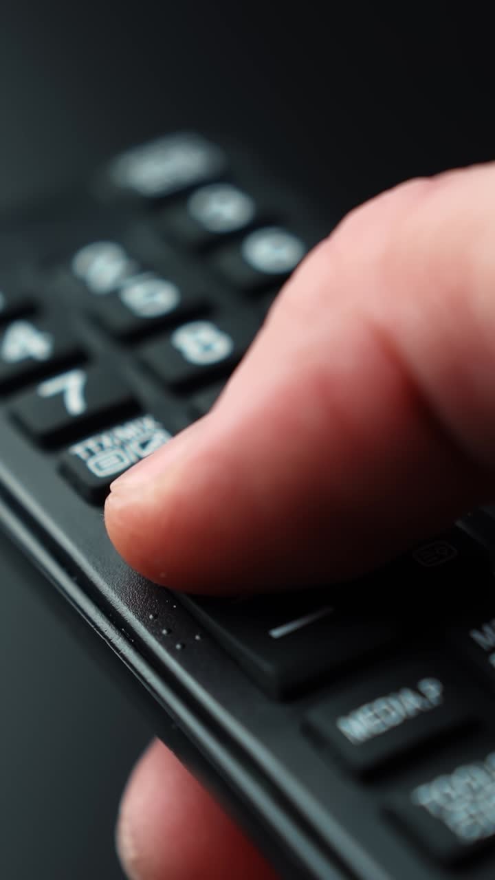 Macro ravvicinata verticale di un dito che preme il tasto più su un telecomando TV per aumentare l'audio, mostrando controlli multimediali tattili per lo streaming di smart TV e l'intrattenimento domestico