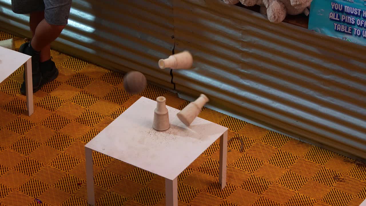 Player throwing a ball, aiming at the milk bottles stacked on the table, a classic carnival knockdown game.