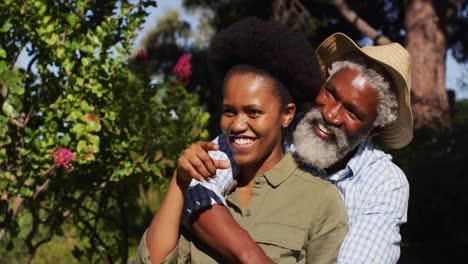 Lächelndes-Afroamerikanisches-Seniorenpaar,-Das-Sich-Im-Sonnigen-Garten-Unterhält-Und-Umarmt