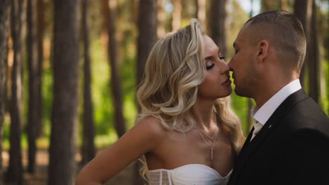 Man-in-classic-suit-and-woman-bride-kiss-standing-in-park