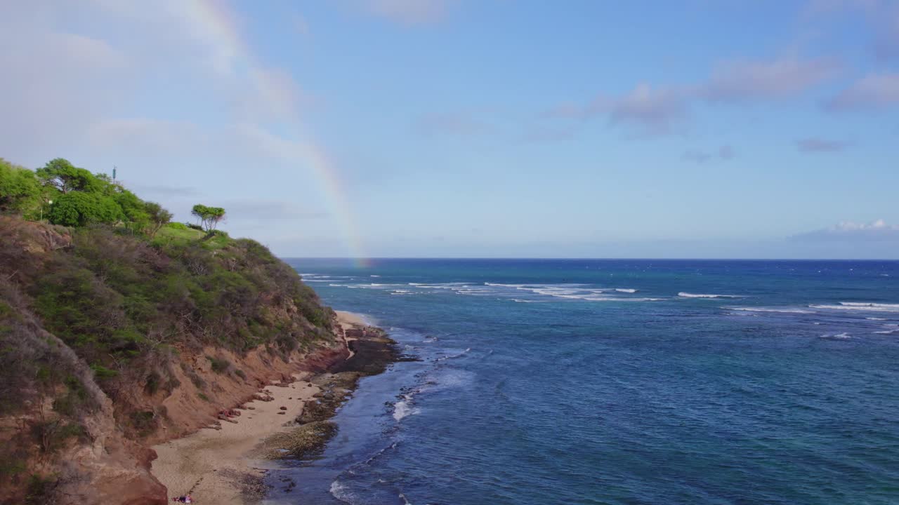 imágenes de drones a lo largo de la costa bordeada de acantilados de la isla de oahu con un arco iris tocando las brillantes aguas azules del océano pacífico