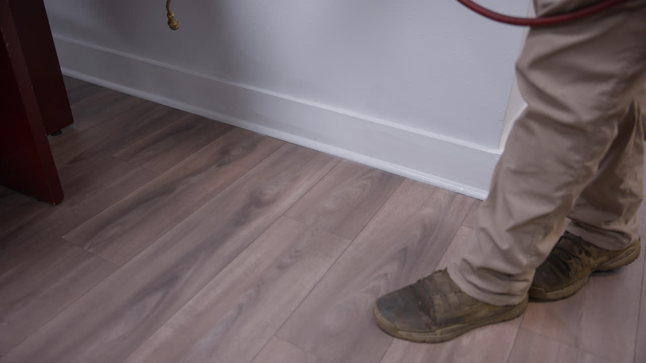 Tracking shot of pest control application being applied indoors along office baseboards and flooring