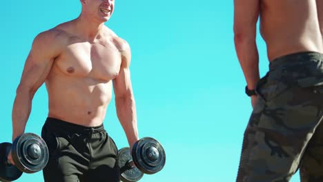 athletes lifting dumbbells on blue sky background. strong sportsmen with muscular body pumping their muscles with weight outdoors.