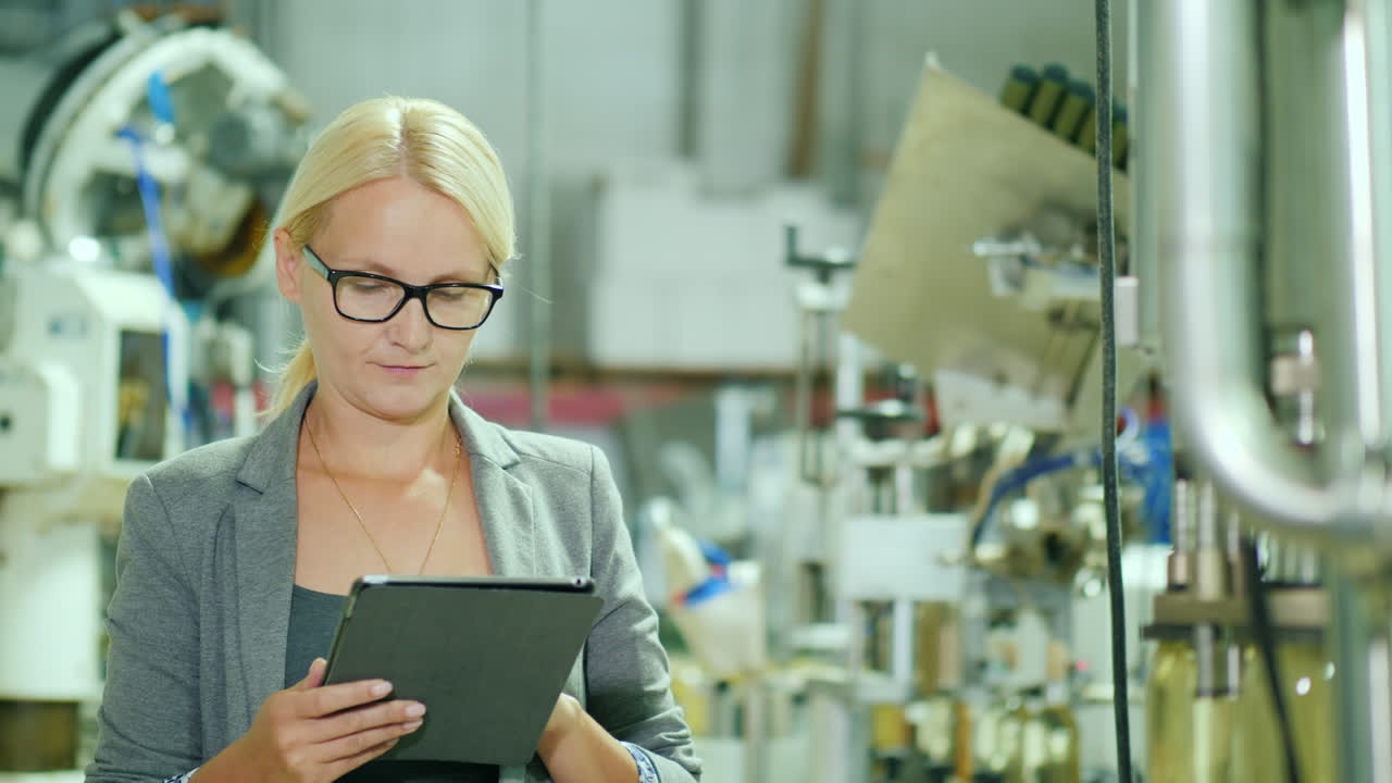 Woman Uses a Tablet by a Bottling Production Line