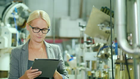 woman uses a tablet by a bottling production line