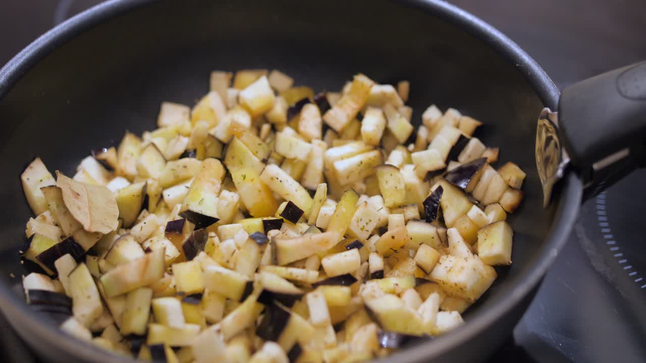 Close up shot of sliced eggplant been cooked in a black frying pan in the kitchen