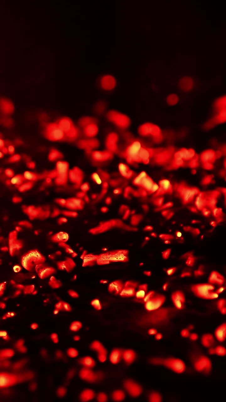 Pile of glowing charcoal after the campfire burnt out. Red pieces of burned wood still hot. Close up. Vertical video