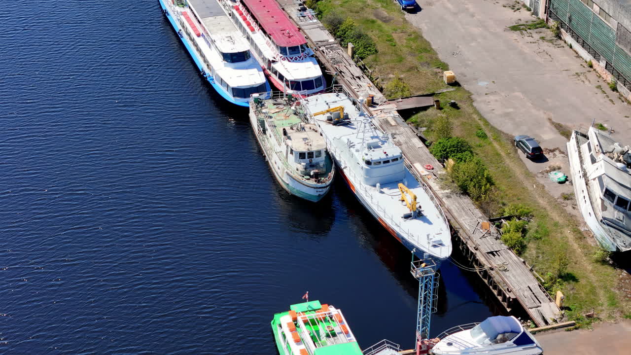 Plano de ángulo ancho de una terminal portuaria comercial y soleada. Un gran buque portacontenedores blanco y rojo está atracado, con su popa mirando hacia la cámara, junto a enormes pilas de contenedores amarillos, rojos y azules.