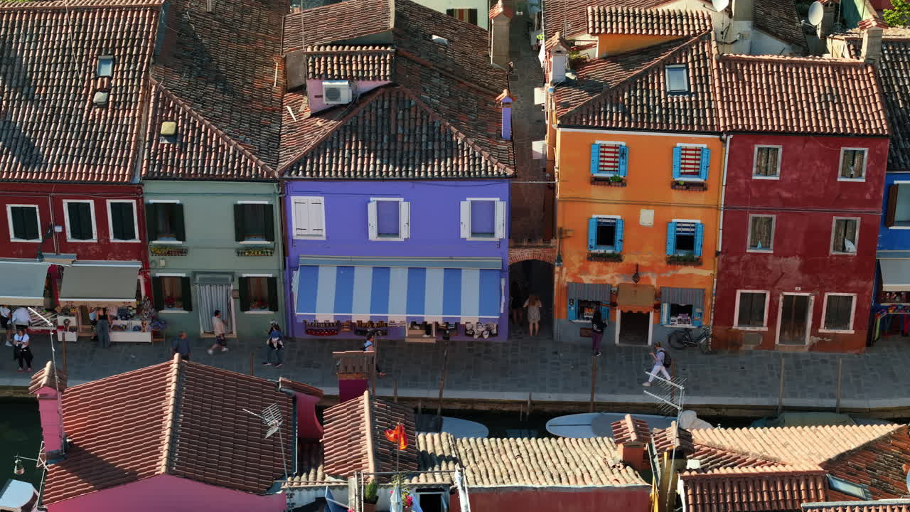 Vista aérea con dron de barcos a los lados de un canal cerca de las coloridas casas de la isla de Burano, Italia