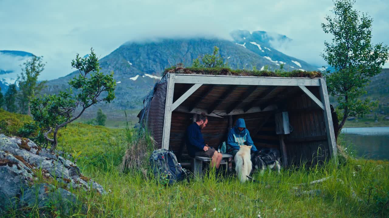 SørTverrfjord, Loppa, Finnmark, Norge - To vandrere hviler med deres hunde ved et lille læskur ved stien under tågede bjerge - Statisk optagelse
