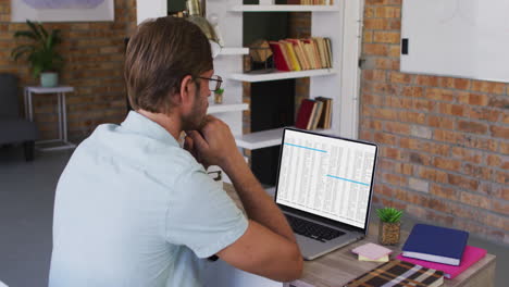 hombre caucásico sentado en el escritorio viendo el procesamiento de datos de codificación en la pantalla del portátil