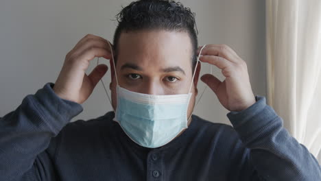 young hispanic male putting on a face mask and looking into camera