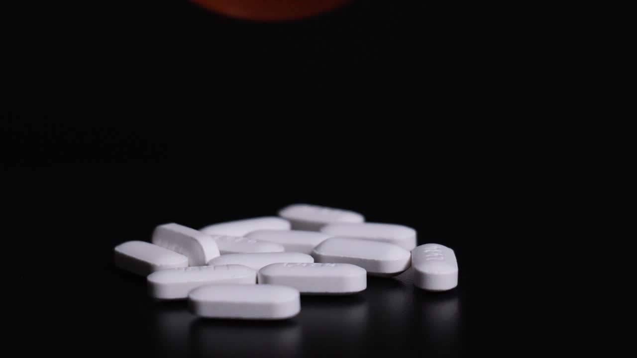 Pillole su prescrizione che fuoriescono da una bottiglia su uno sfondo scuro
