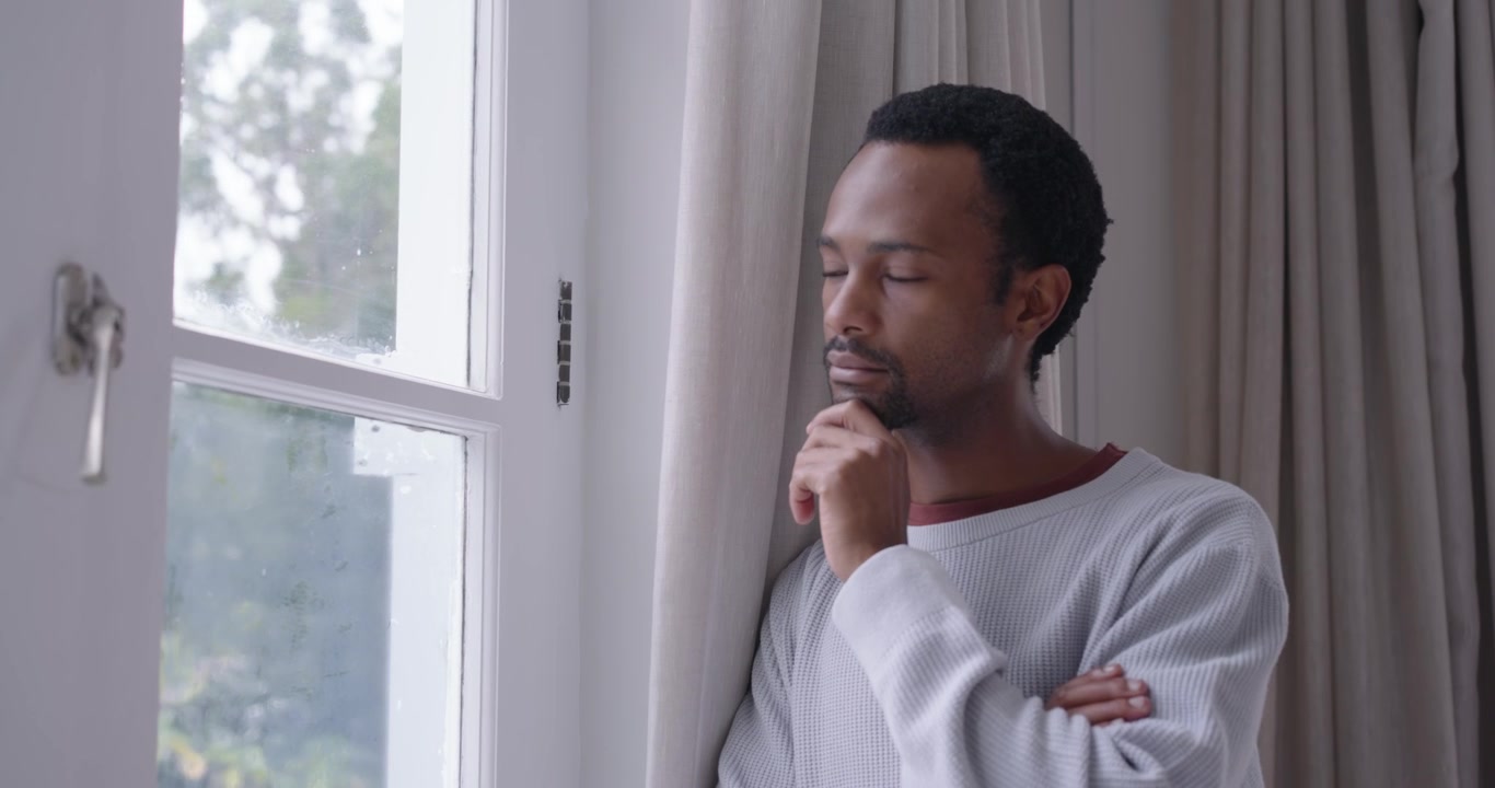 African American adult leaning by paned window, dim light urging shifting gaze, closing, looking