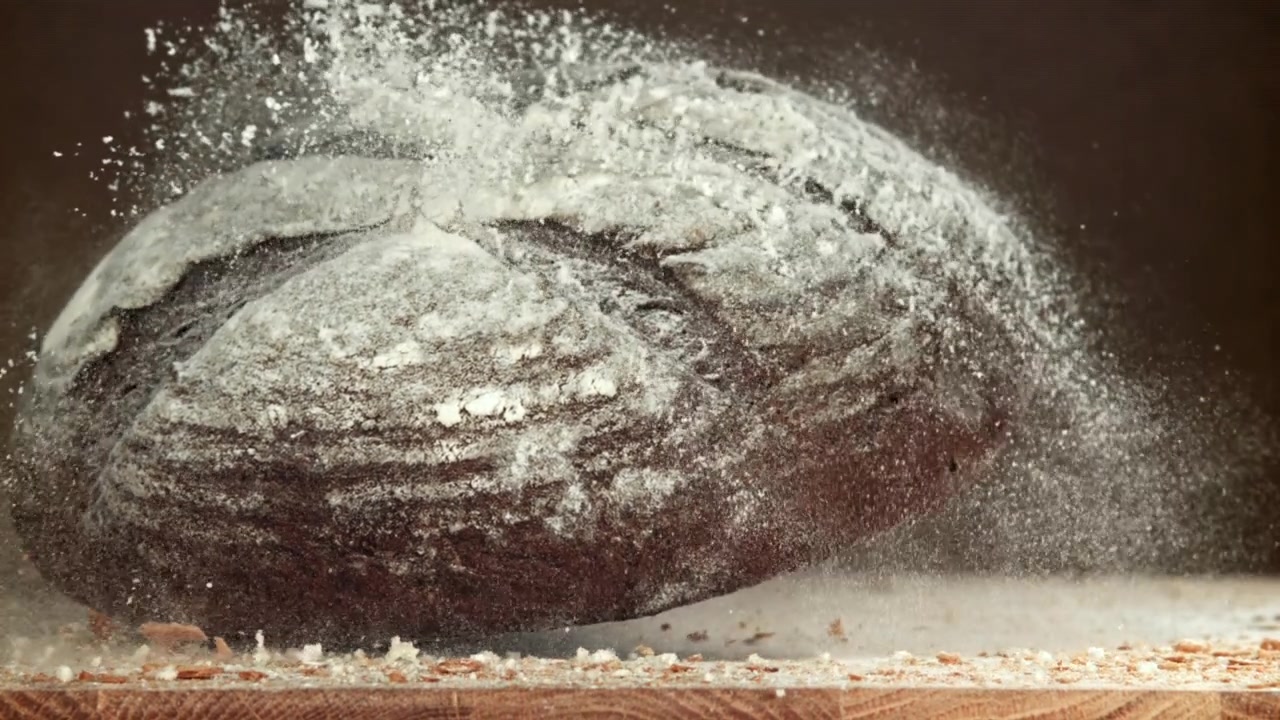 Versgebakken roggebrood dat in slow motion op een houten tafel neerkomt