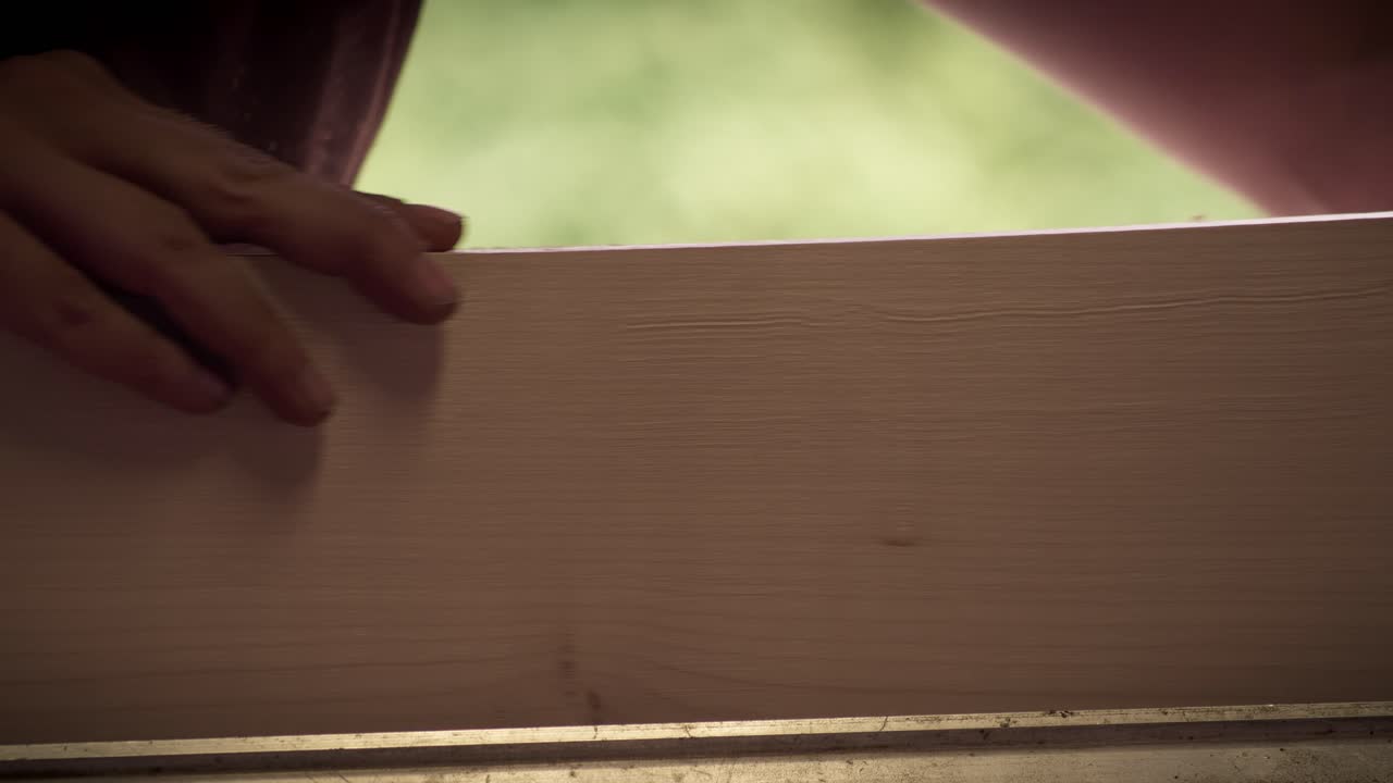 Una falegname donna controlla la finitura di un'asse chiara passando la mano lungo il bordo. Primo piano, slow motion.