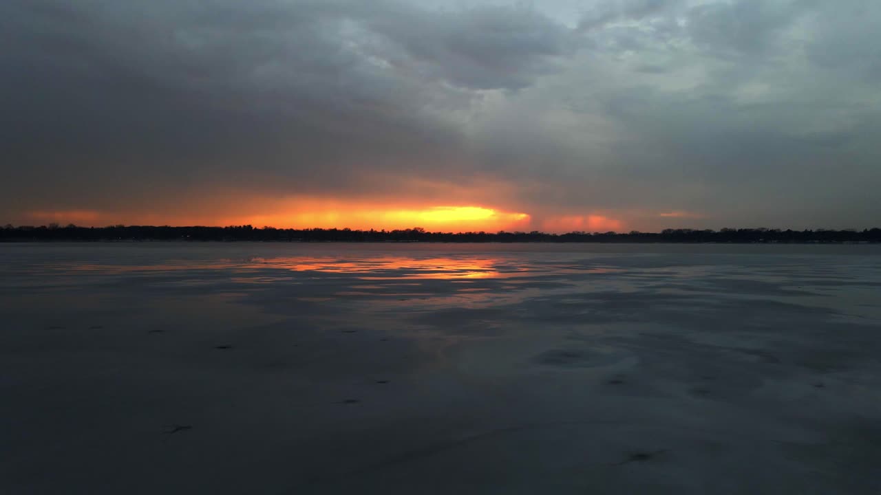Beeindruckende Farben an den Wolken während des Sonnenuntergangs über einem zugefrorenen See in Minnesota.