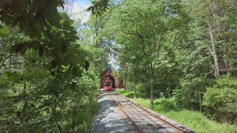 a restored antique steam engine, approaching, riding along a single track in the woods on a sunny day