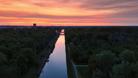 breathtaking colorful sky at sunset reflects in the mirror surface of canal. lush green forests grow around the canal. aerial view.