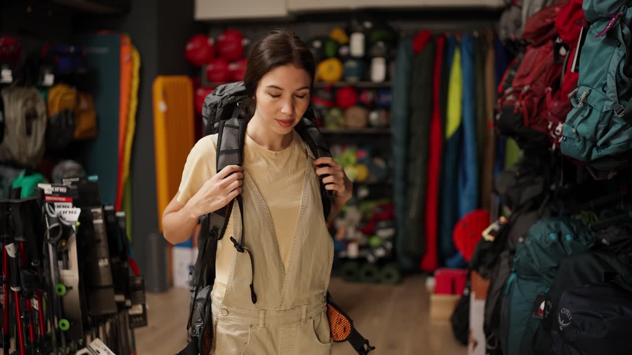 mujer joven intentando una mochila turística grande en una tienda de equipos deportivos, cámara lenta