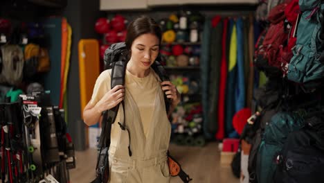 Young-woman-trying-big-tourist-rucksack-in-sports-equipment-store,-slow-motion