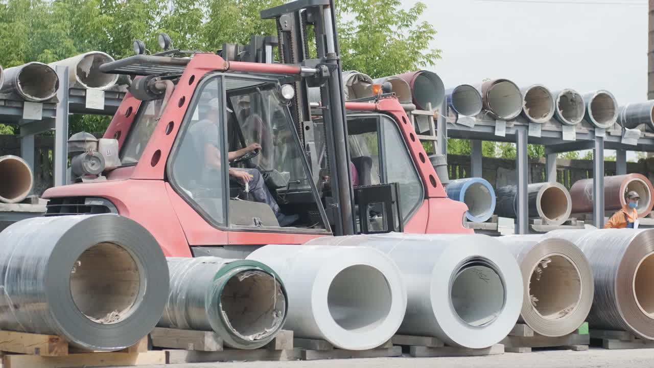 el conductor de la carretilla elevadora carga rollos de chapa de acero. almacén industrial con rollos de láminas de acero