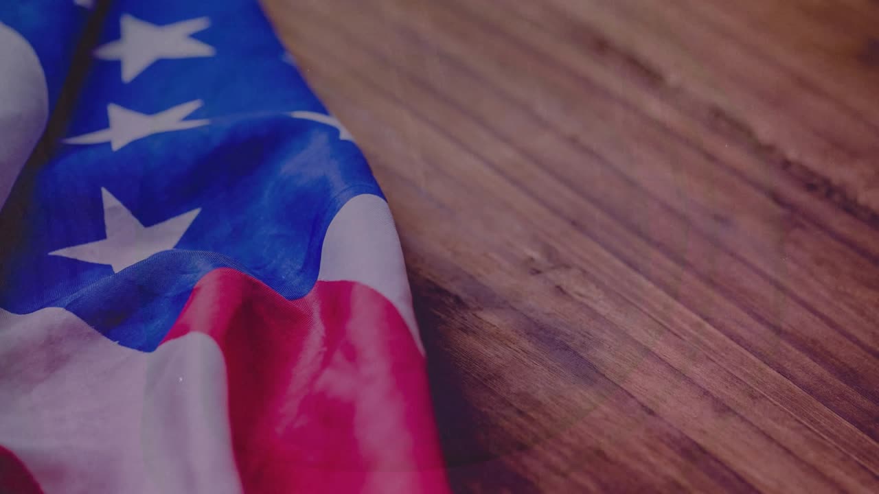 Film grain flickering causing light specks drifting across US flag cloth on wood evoking nostalgia