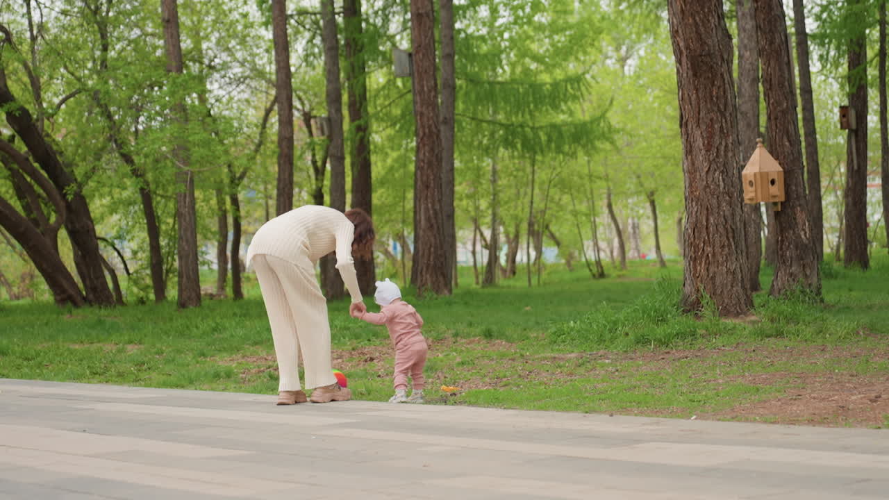 Caucasian Grandmother Guiding Toddler On Paved Path In Green Park, Gentle HandHold, Colorful Ball At Side, Birdhouse On Tree, Warm Spring Light, Patient Teaching First Steps, Emotional Generational