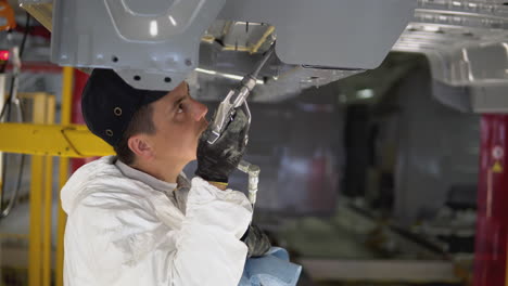 trabajador inspeccionando la parte inferior de un vehículo en un taller de pintura
