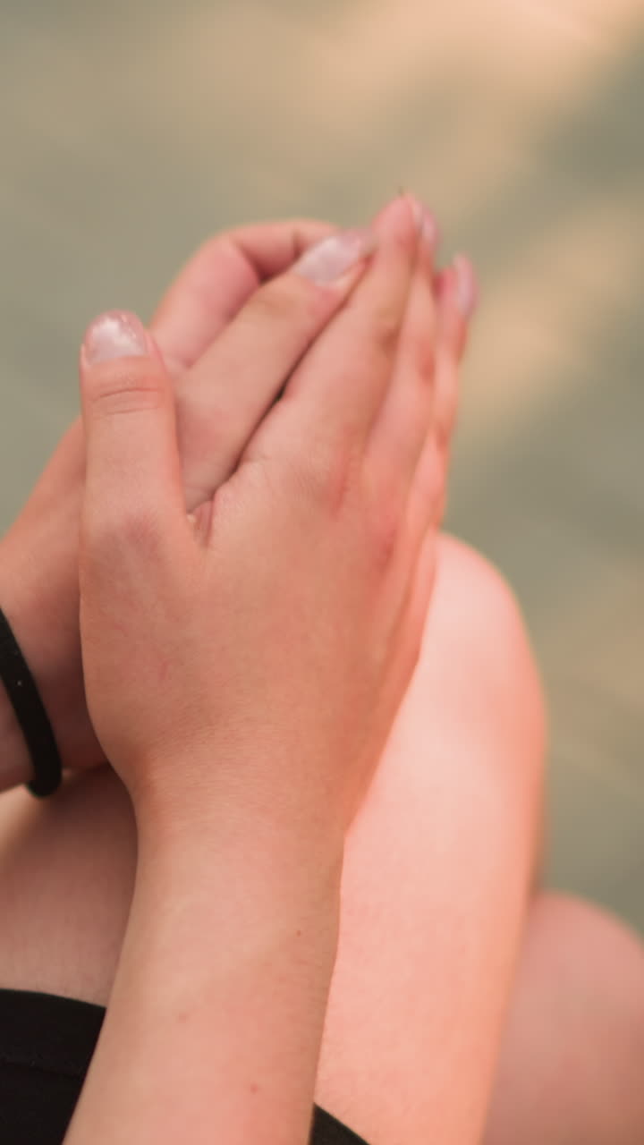 vista parcial de una dama sentada al aire libre con las piernas cruzadas, las manos apoyadas en la rodilla mientras frotan suavemente las palmas bajo la cálida luz del sol, fondo suavemente borroso