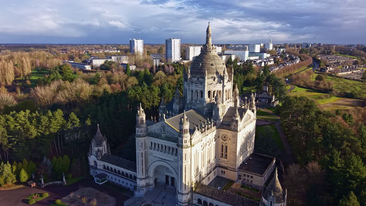 Um drone se afasta em arco, revelando a basílica iluminada pelo sol de Lisieux e a cidade na Normandia
