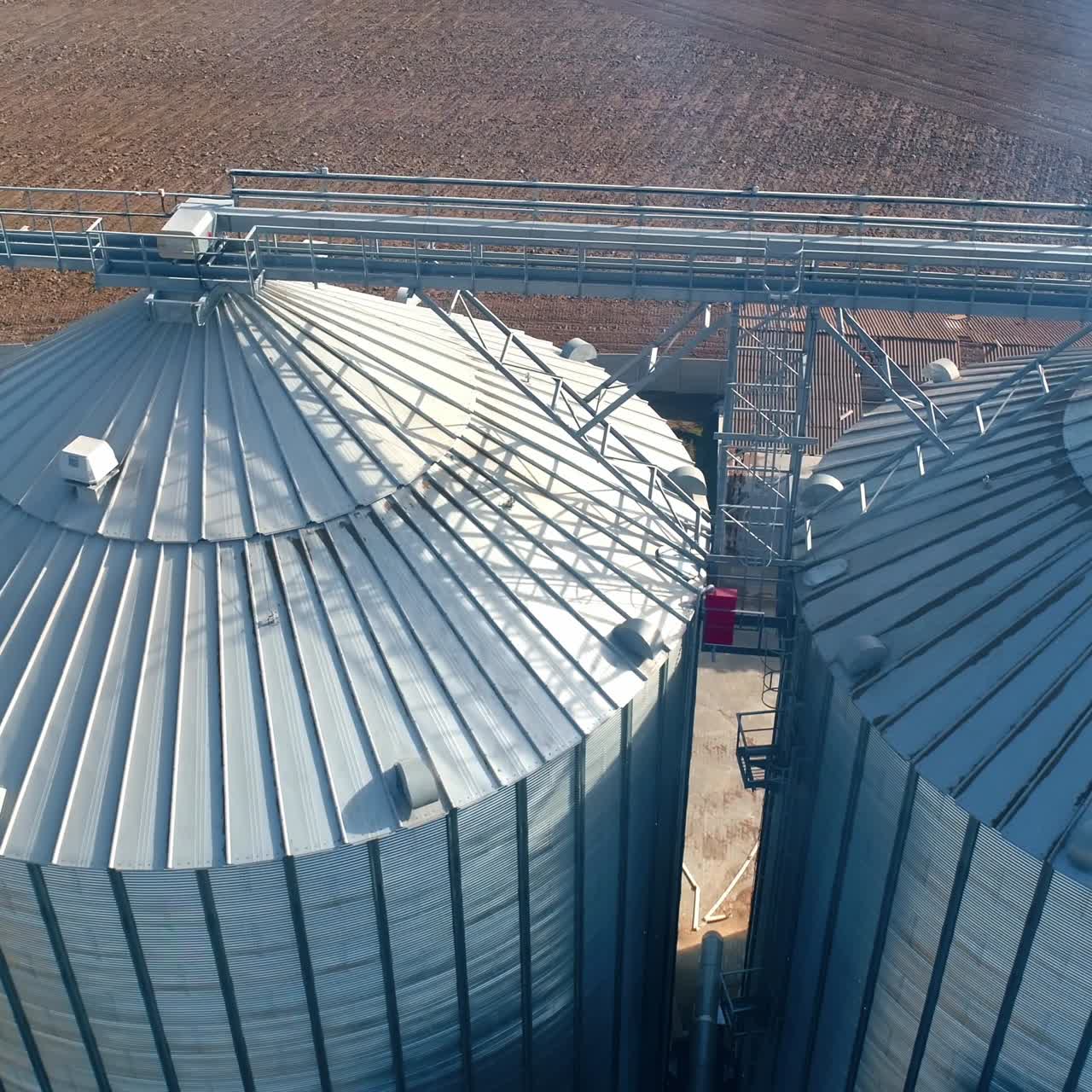 Metal silos on field. Large containers for storing and processing grains. Silver grain elevators in farmland. Aerial view.