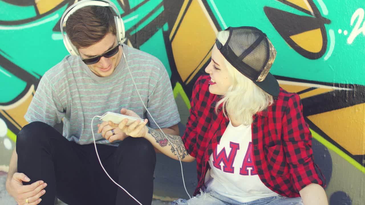 una divertida pareja de jóvenes hipsters escuchando música.