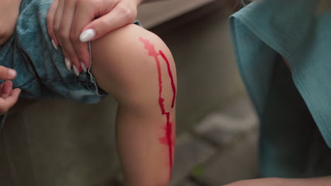 a close-up of a woman s hand with manicured nails gently cleaning a child's leg with a tissue, which is stained with blood