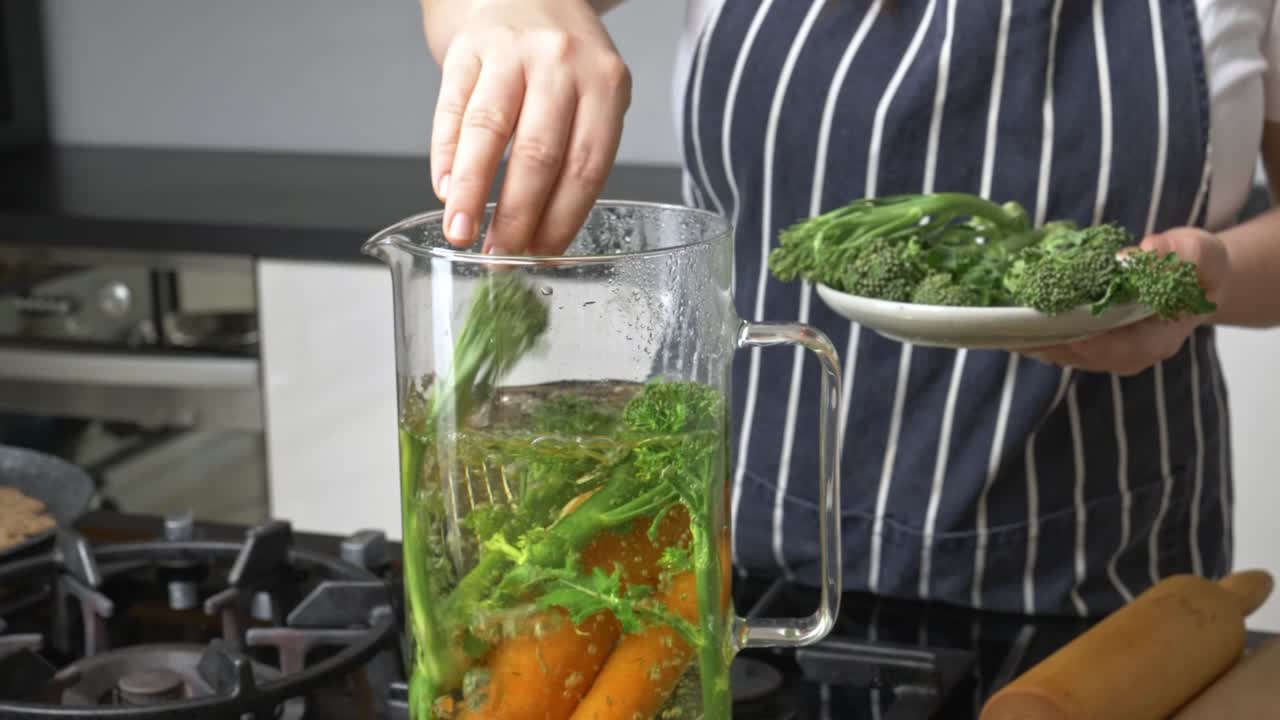 Chef prepares vegetables in a pitcher of boiling water with a plate of broccoli
