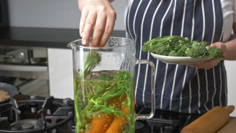 chef prepares vegetables in a pitcher of boiling water with a plate of broccoli