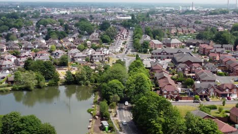 Establishing-aerial-view-zoom-in-towards-detached-neighbourhood-property-and-lakeside-red-brick-British-townhouse-building-site