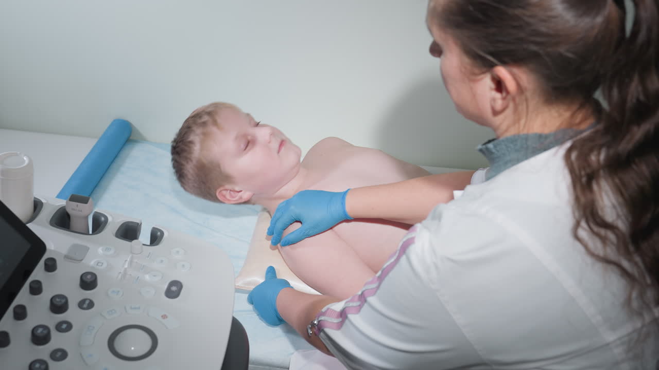 Medical staff in lab coat wearing examination gloves gently supports patient to raise head while adjusting position, then turns back to diagnostic machine to resume checkup in clinical environment
