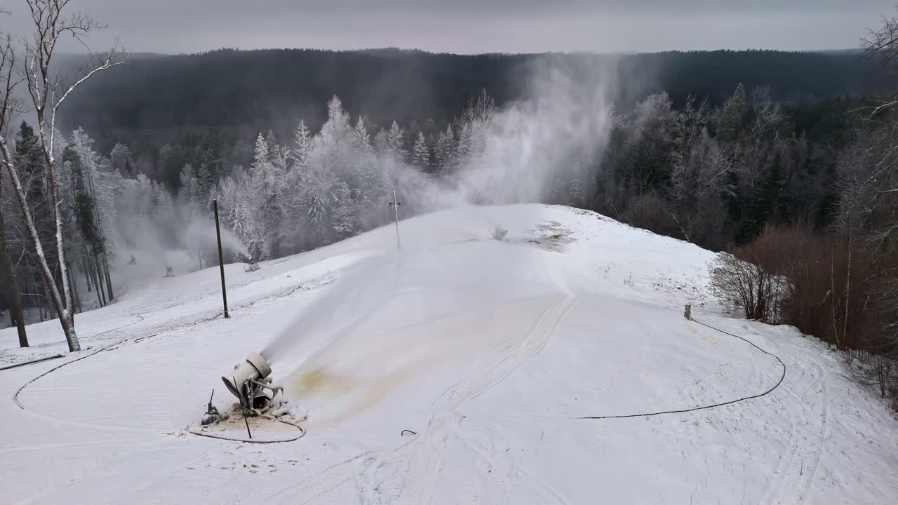 Vista aerea con drone di cannoni da neve in funzione su una pista da sci innevata circondata da una foresta