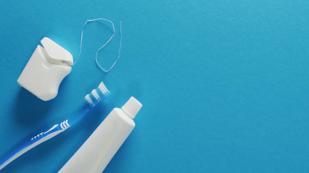 Video of close up of toothbrush, paste and floss on blue background
