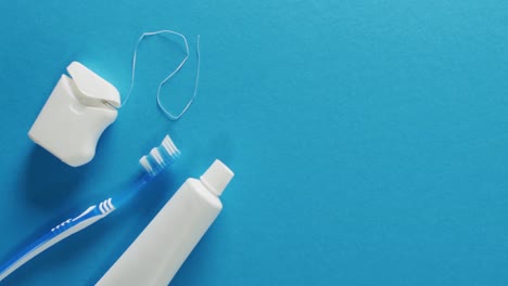 Video-of-close-up-of-toothbrush,-paste-and-floss-on-blue-background