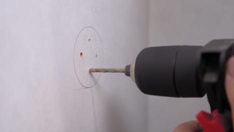 husband or handyman drills holes in surface of wall according to a pencil drawing to insert bolts and hang shelf or hooks, install furniture, close up.