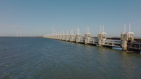 Aerial-shot-zooming-in-on-and-flying-over-the-Eastern-Scheldt-storm-surge-barrier-in-Zeeland,-the-Netherlands,-on-a-beautiful-sunny-day