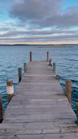 vertical - cloudy sunset sky over lake with wooden jetty in foreground